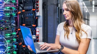 Frau mit Laptop vor Serverwand