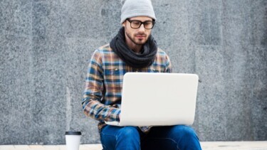 Mann sitzt auf Stufe und arbeiten draußen am Laptop