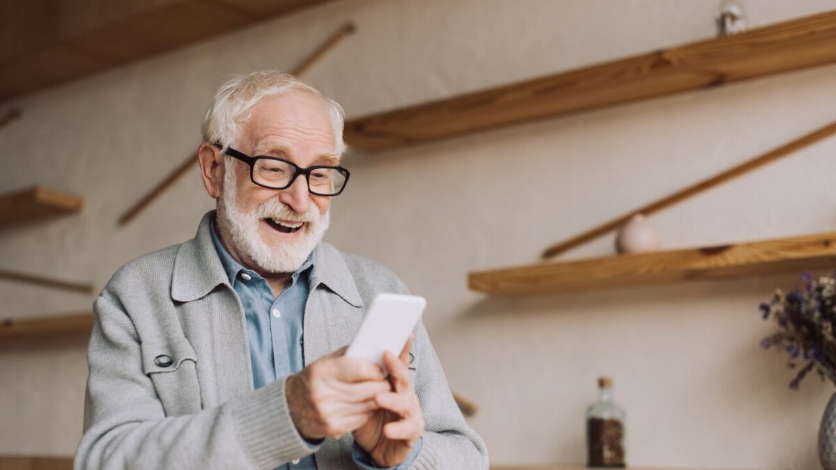 Weißhaariger Mann mit Brille mit Smartphone in der Hand