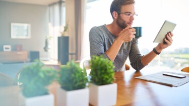 Junger Mann trinkt Kaffee während er auf seinem Tablet liest